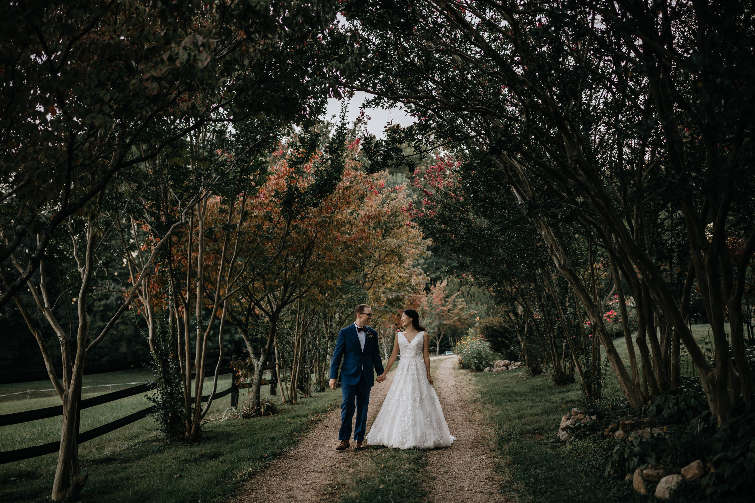 bride and groom walking down a dirt road under a canopy of trees at storybrook farms