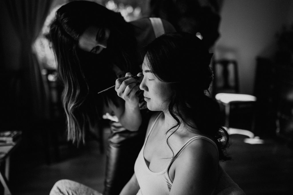 bride getting makeup on in black and white
