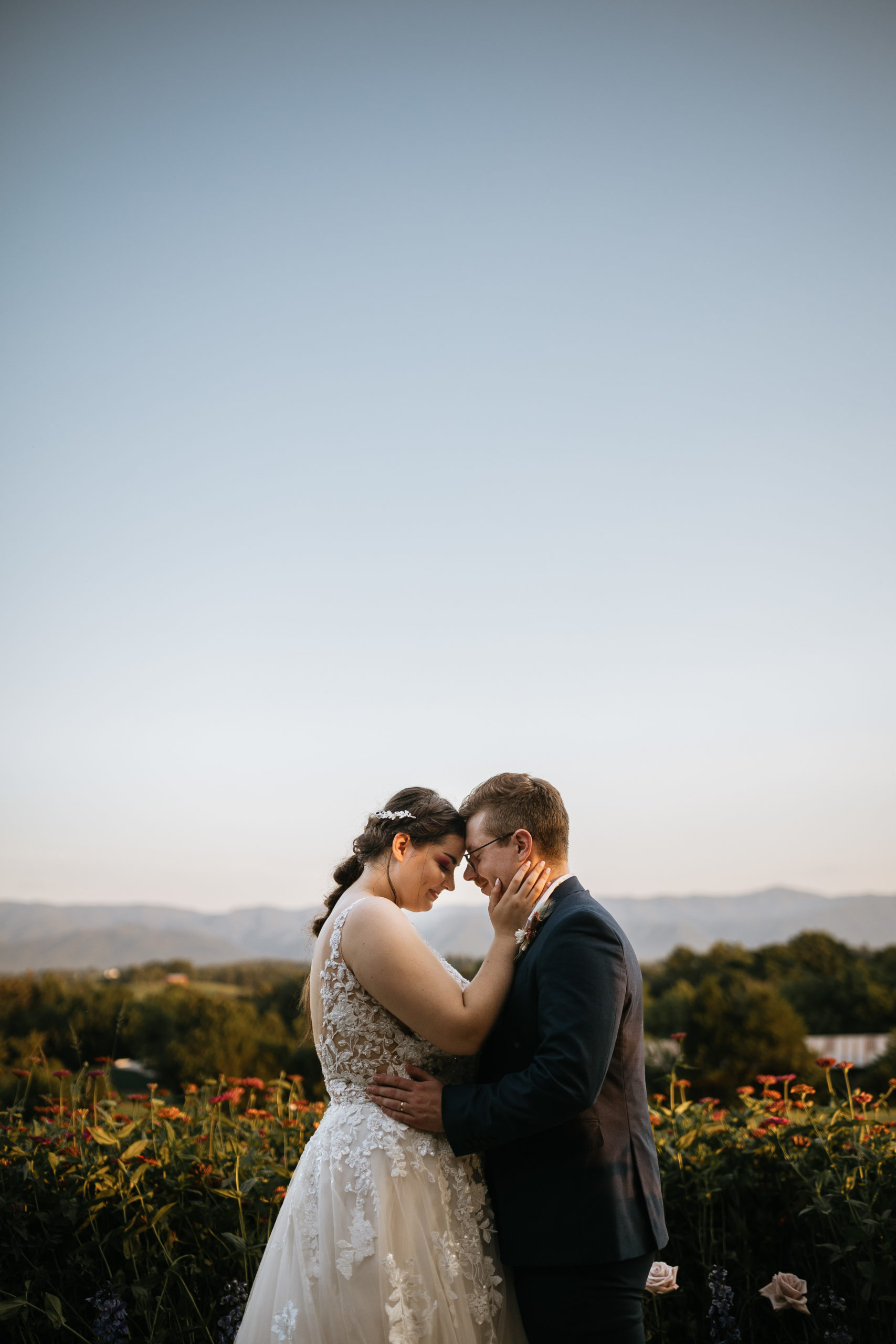 bride and groom standing with their foreheads together on top of a mountain with wildflowers behind them