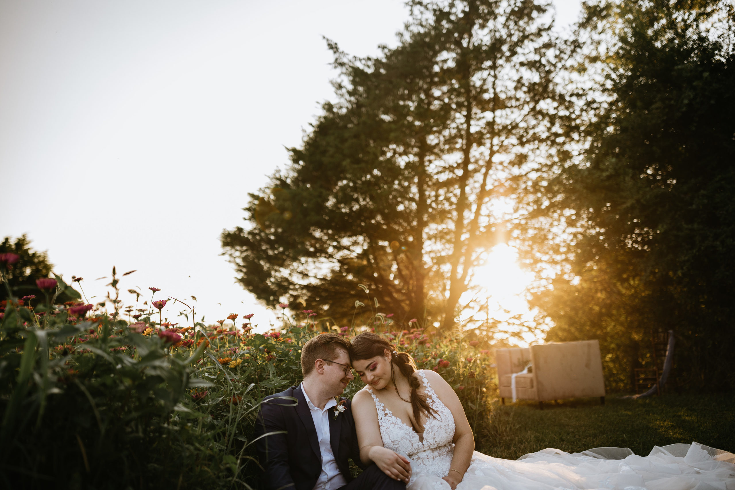 bride and groom cuddled on the ground in front of wildflowers during sunset at greenwood oaks