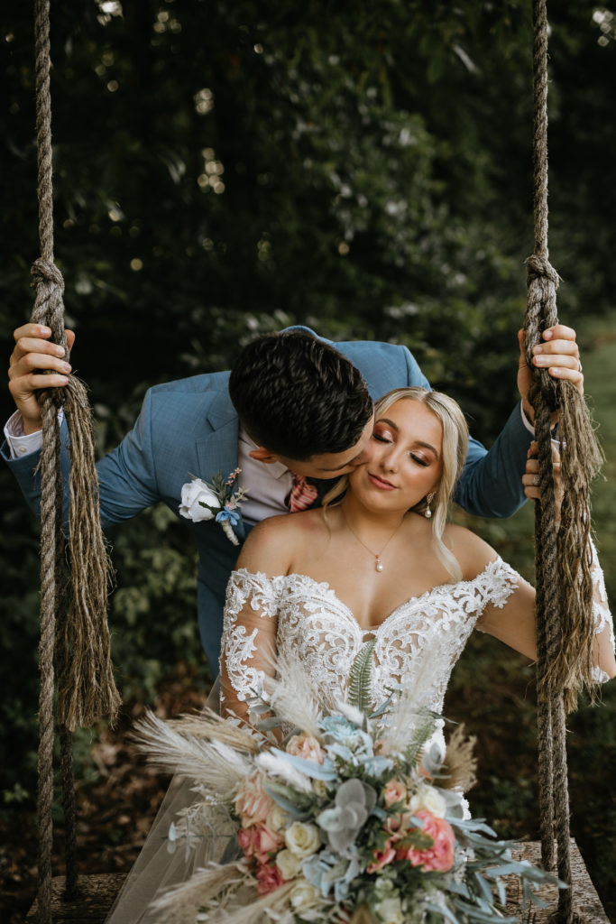 bride and groom on swing and groom kissing cheek
