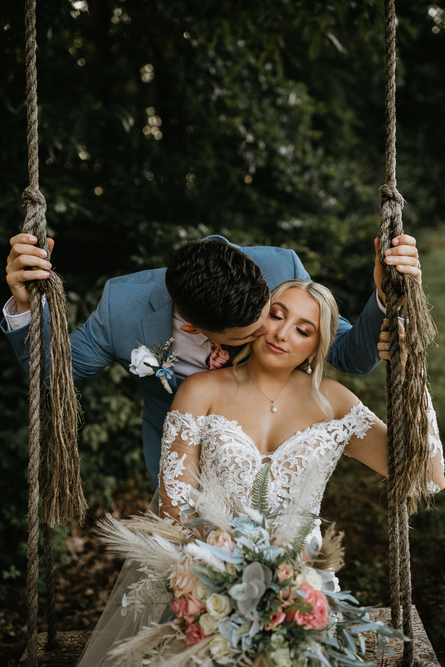 bride sitting on swing groom behind her kissing her cheek