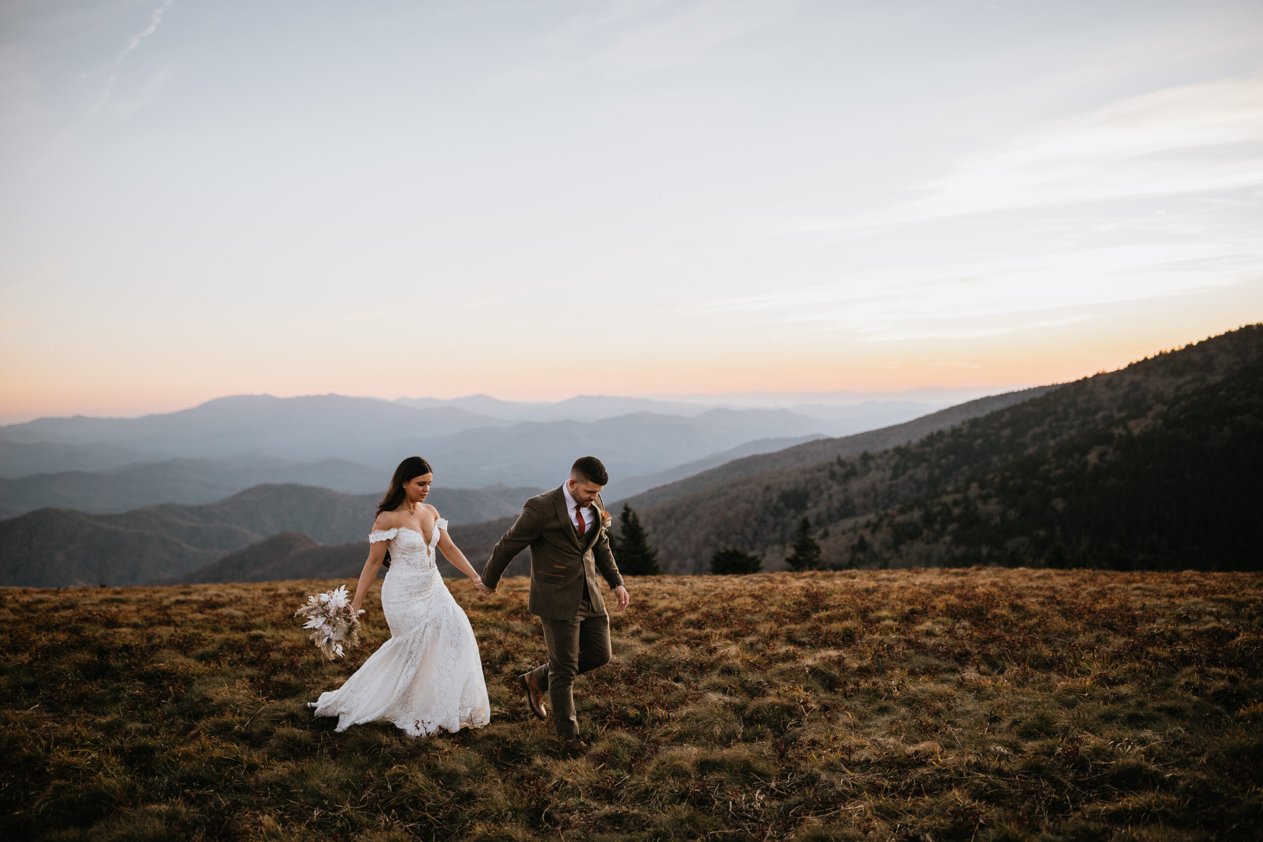 groom leading bride on top of mountain with beautiful mountain views in the background
