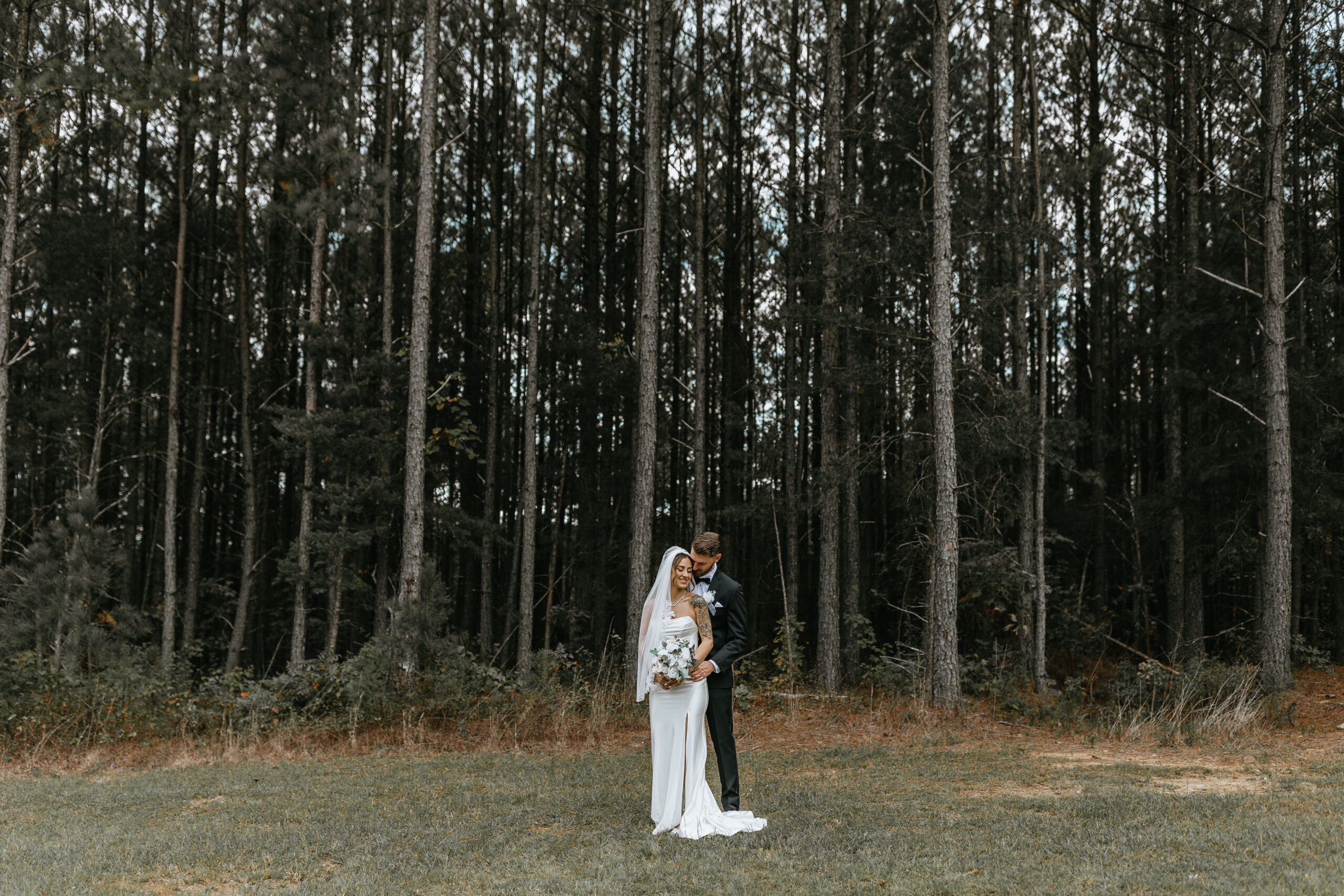 bride and groom stand hugging in front of pine tree forest during intimate wedding at chattanooga airbnb