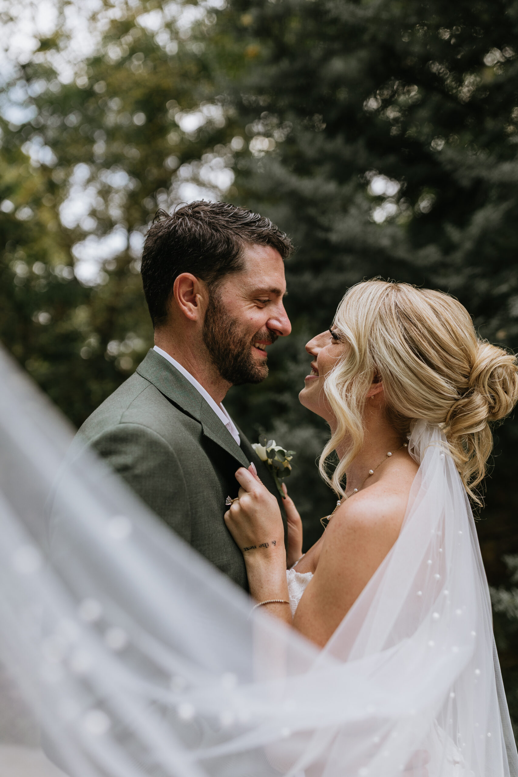 bride and groom stand and smile at each other as brides veil is in foreground of image during their waterstone wedding